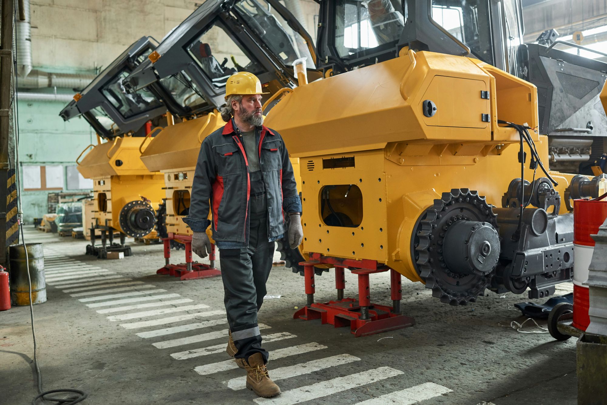 Man in a hard hat in a construction workshop walking next to some vehicles