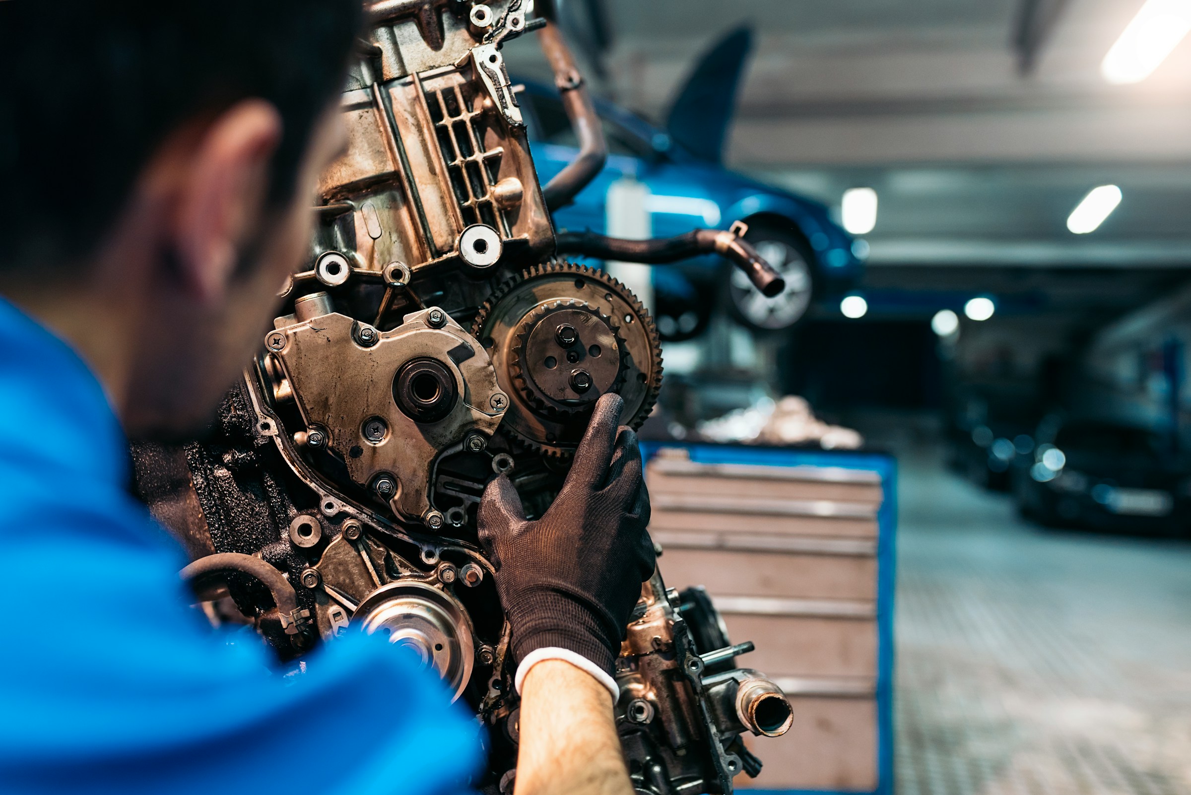 A mechanic in gloves working on an oily engine